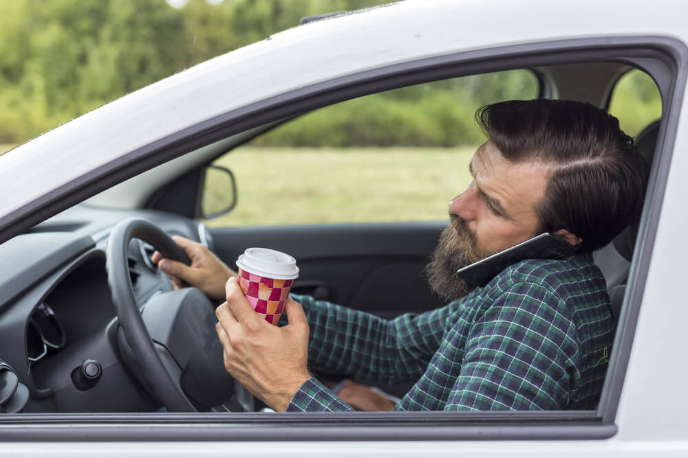 Distracted driver talking on the phone while his other hand holds a cup of coffee.