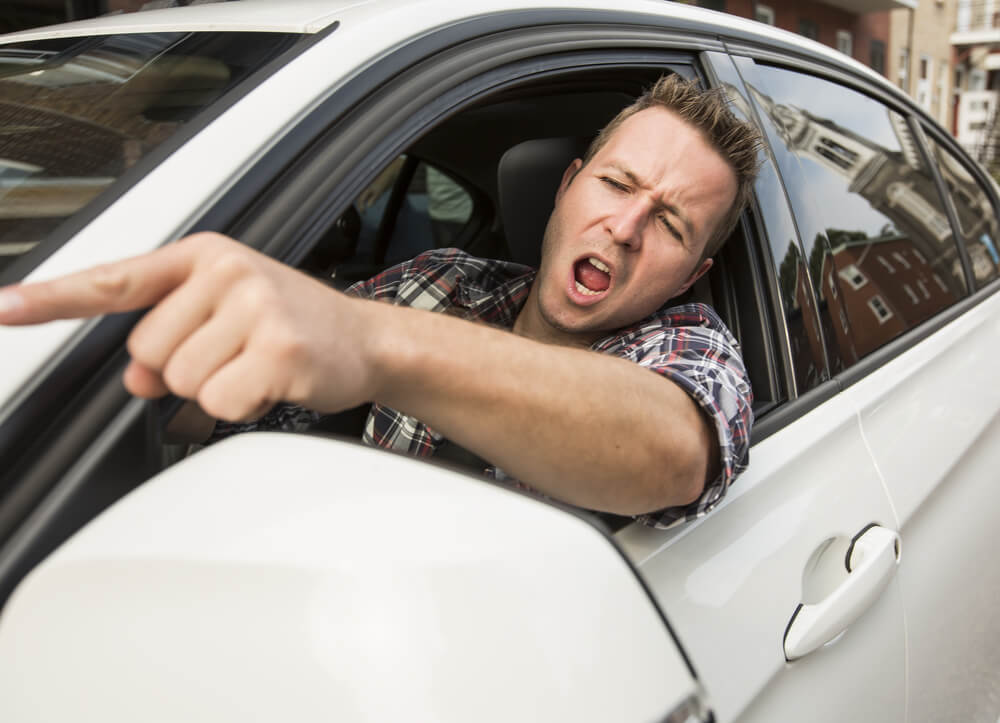 Angry driver pointing at car in front of him. This distraction can cause an accident.